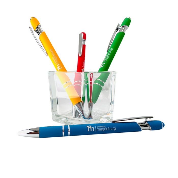 Bunte Kugelschreiber mit Touch-Spitze, markiert mit 'ottostadt magdeburg', in einem Glasbehälter. Stifte in Blau, Gelb, Rot und Grün.
