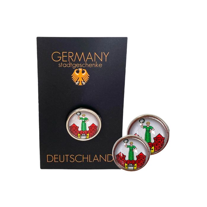 Pin mit dem Stadtwappen von Magdeburg, präsentiert auf schwarzem Hintergrund mit goldener Schrift 'Germany Stadtgeschenke'. Der Pin zeigt eine grüne Figur auf einem roten Hintergrund, typisch für das Magdeburger Wappen. Dieses Souvenir ist als Deutschland Stadtgeschenk gekennzeichnet.