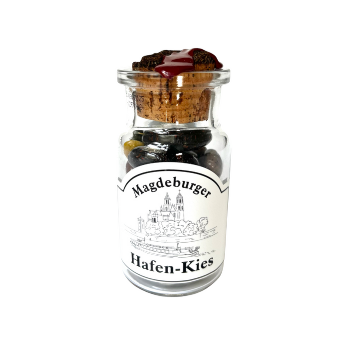 Ein Glasbehälter mit der Aufschrift 'Magdeburger Hafen-Kies', gefüllt mit bunten Steinen und versiegelt mit einem Korken, Magdeburg-Shop.